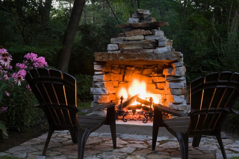 A stone firepit in a backyard with lawn chairs in front of it.