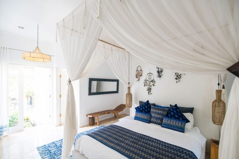 A blue and white bedspread with a white bed canopy hanging above it.