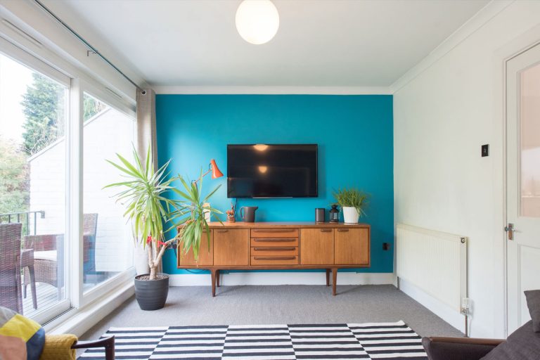 A living room, with a bright blue wall that has a TV mounted in the middle of it.