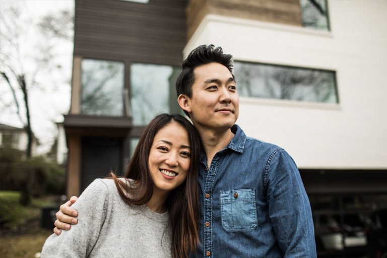 A smiling couple standing in front of their house.