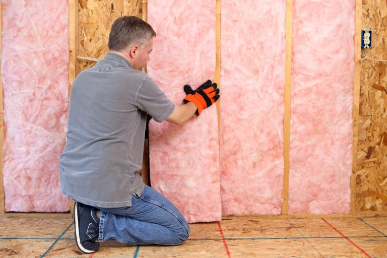 A person installing pink insulation into the wall of a house.