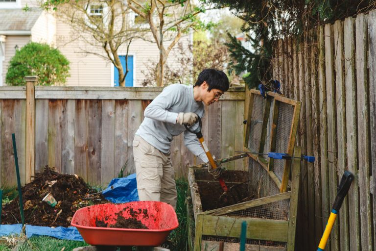 A man putting soil in a compost bin in a backyard.