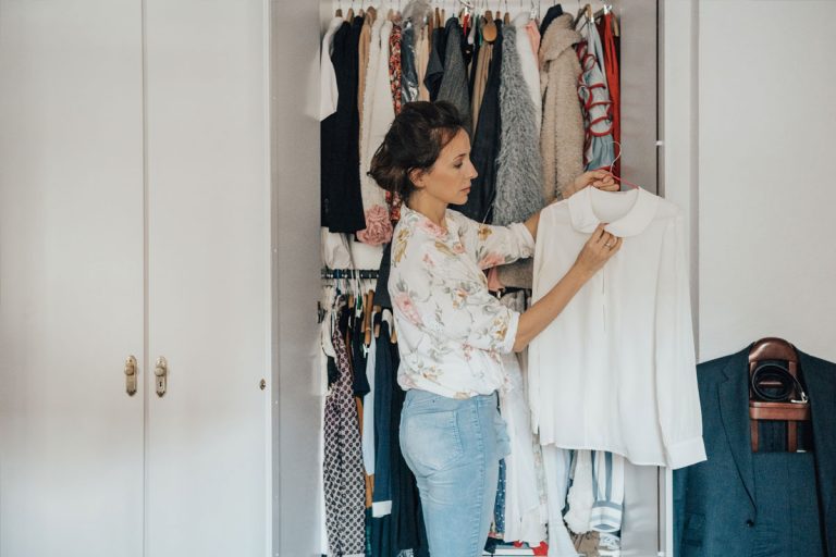 A woman hanging up shirts in a closet.