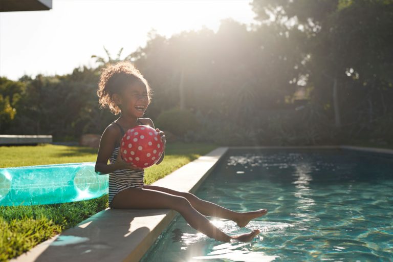 A little girl sitting on the side of an inground pool.