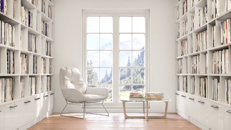 A room lined with white bookcases and a white chair in the middle.