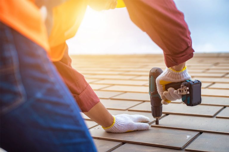 A person drilling a shingle on a roof.