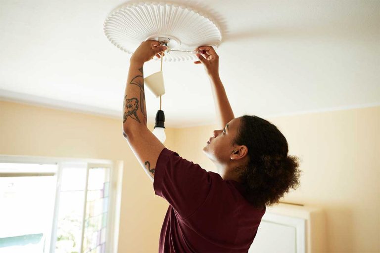 A woman installing a light fixture.