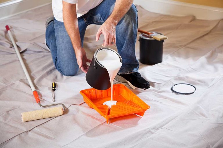 A painter pouring paint into a plastic paint tray.