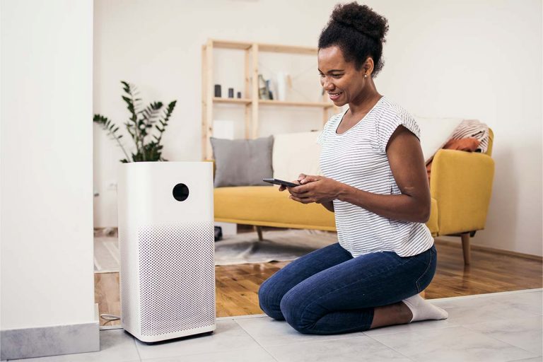 A person sitting in their living room next to an air purifier.