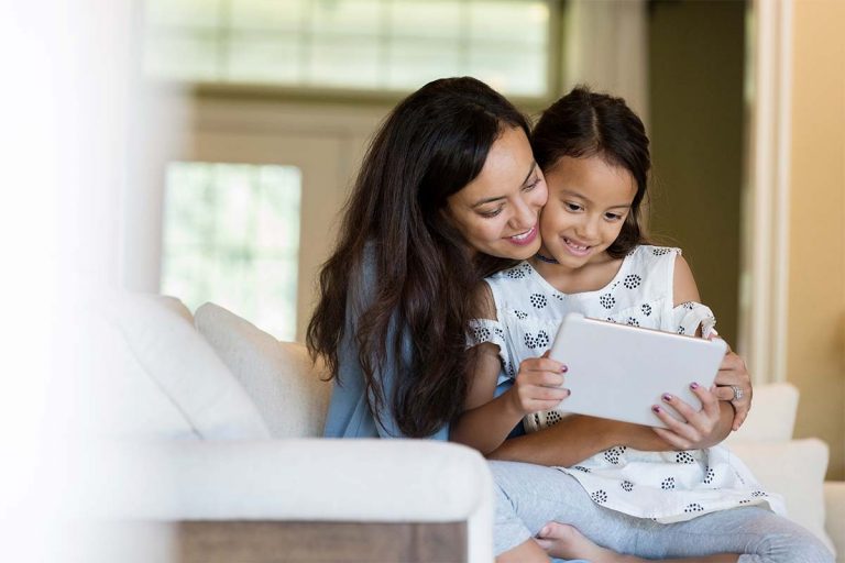 A daughter sitting on her mom's lap with an iPad.