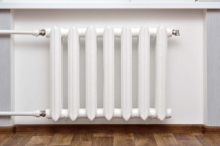 A white cast iron radiator attached to a white wall.
