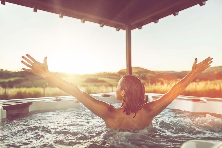 A woman in an outdoor hot tub extending her arms in the air.