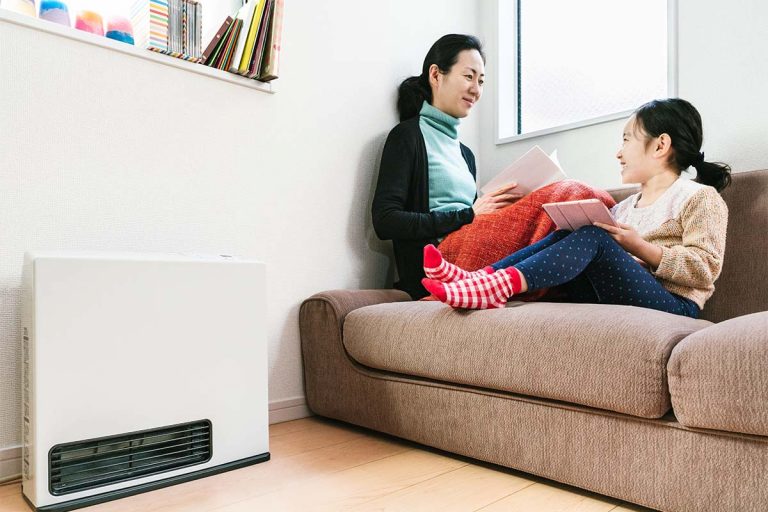 A mom and child sitting on a couch next to a portable air conditioner and heater.