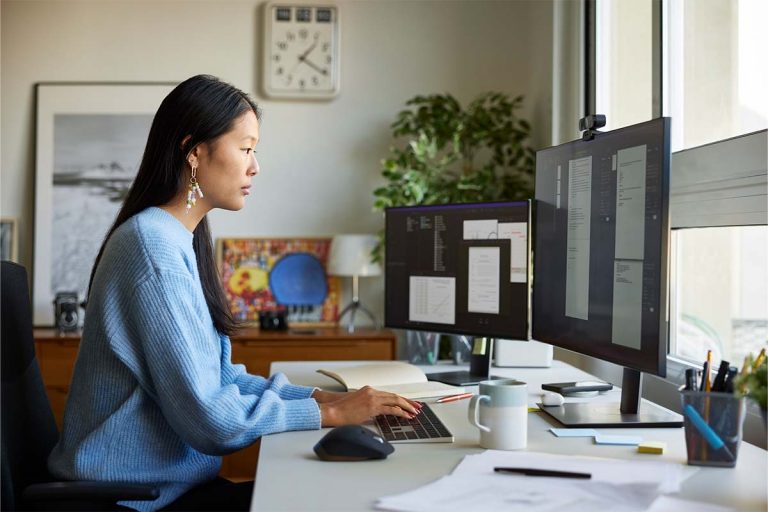 A woman sitting at a desk at home working in front of computers.